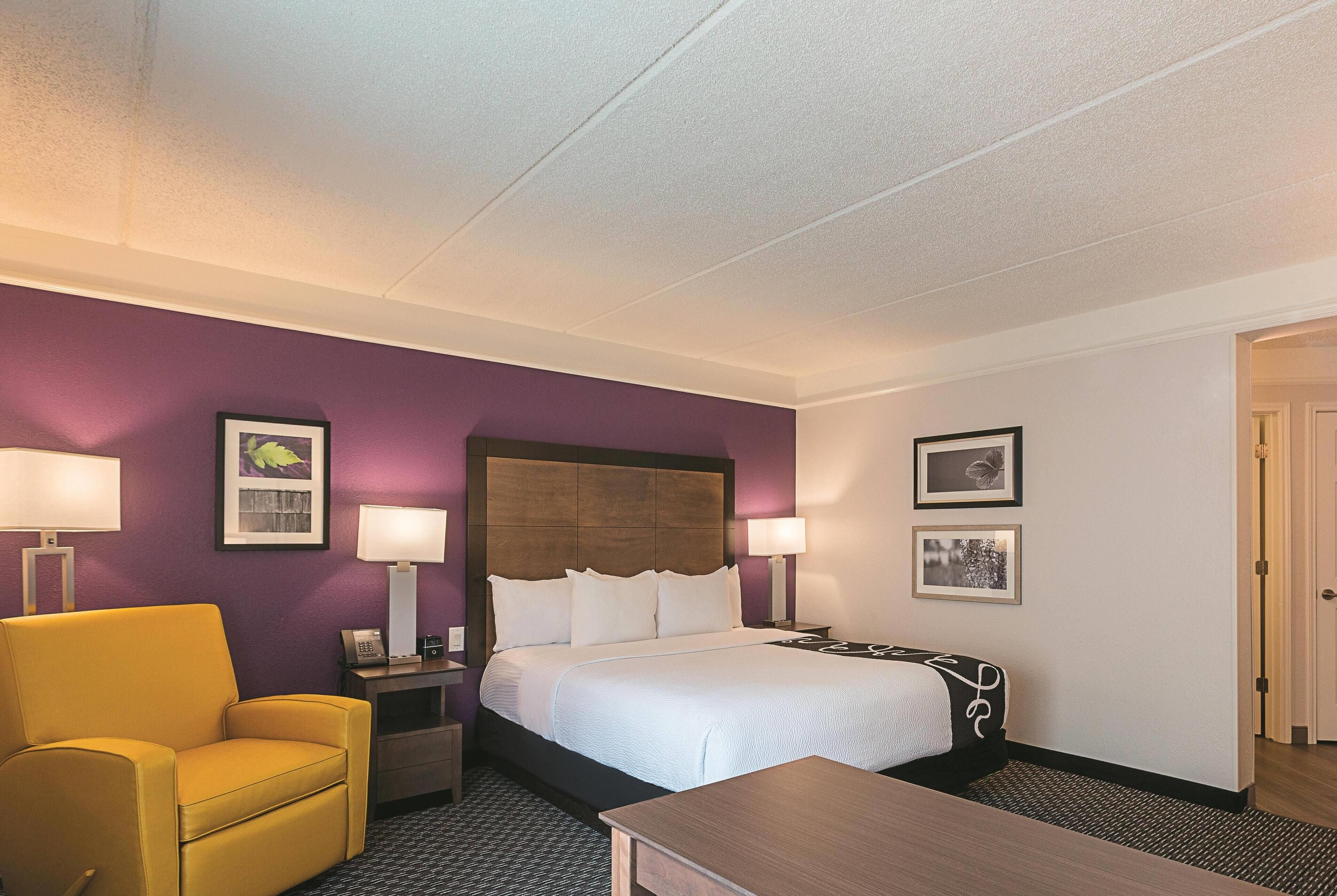Habitación de hotel con una cama grande, un sillón amarillo, una mesita de noche con lámpara y un escritorio.