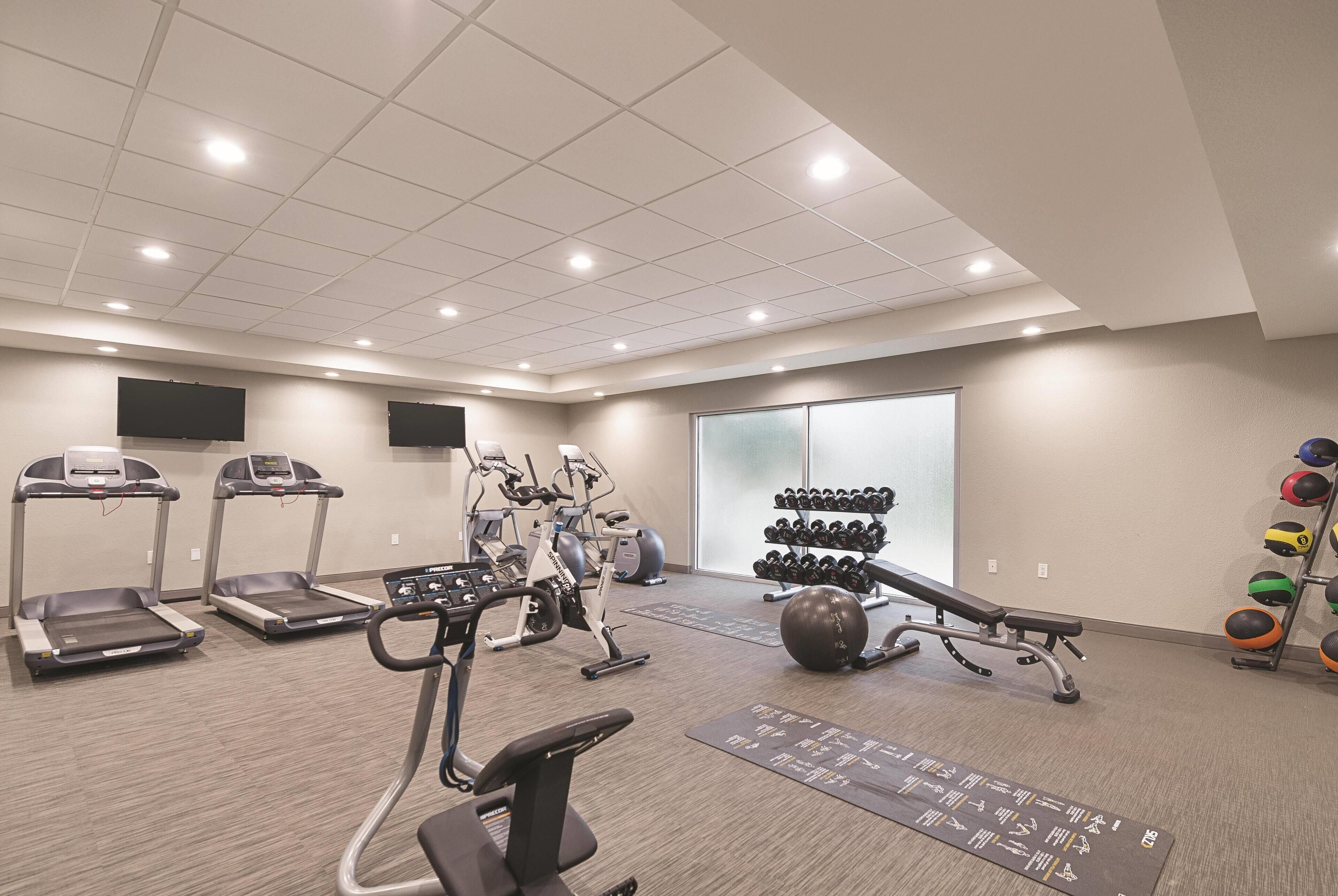 Une salle de sport équipée de tapis de course, de vélos elliptiques, d’un banc de développé couché, d’haltères et de ballons d’exercice.