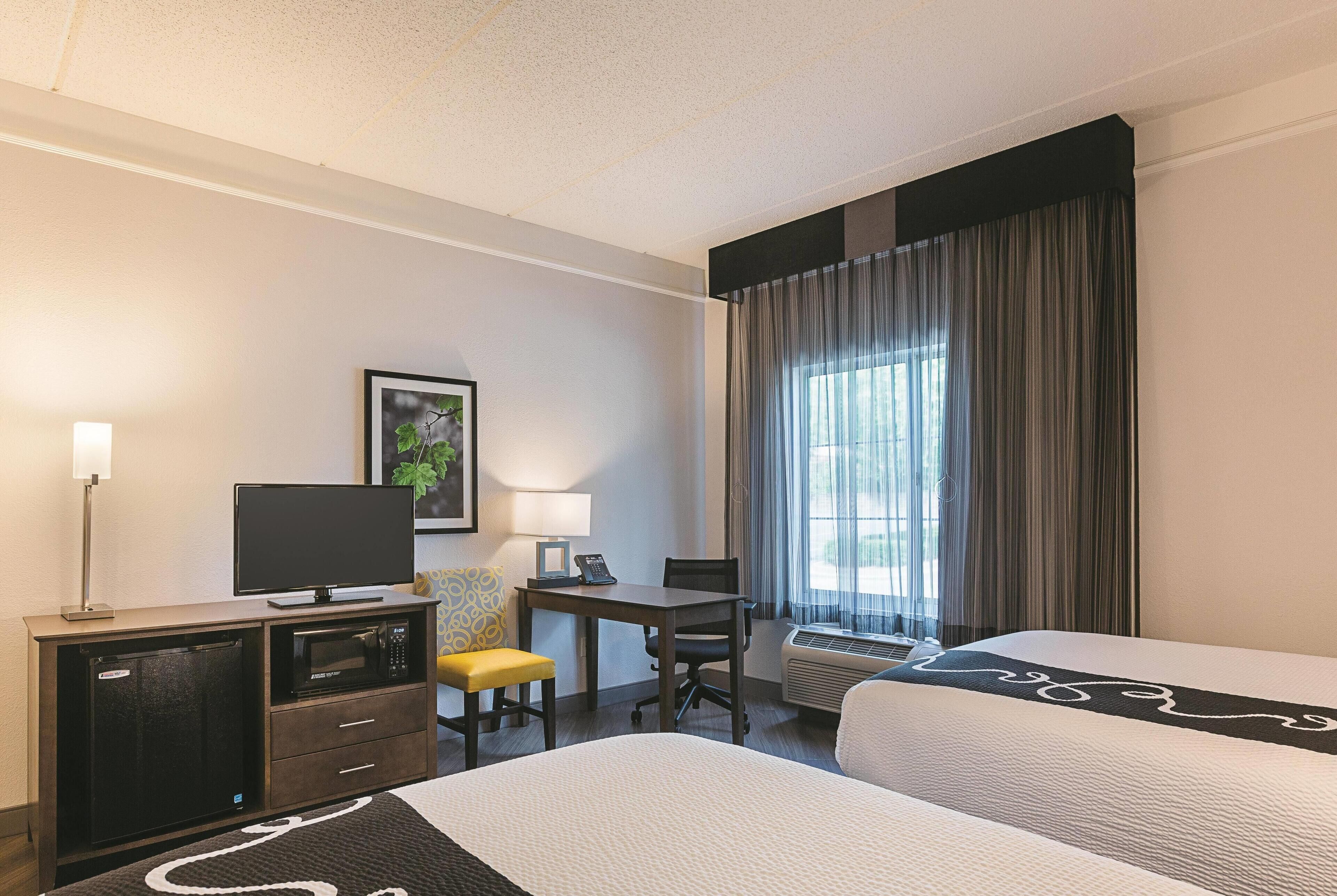 Hotelkamer met een bed, een bureau met een computer, een magnetron, een stoel en een airconditioning.