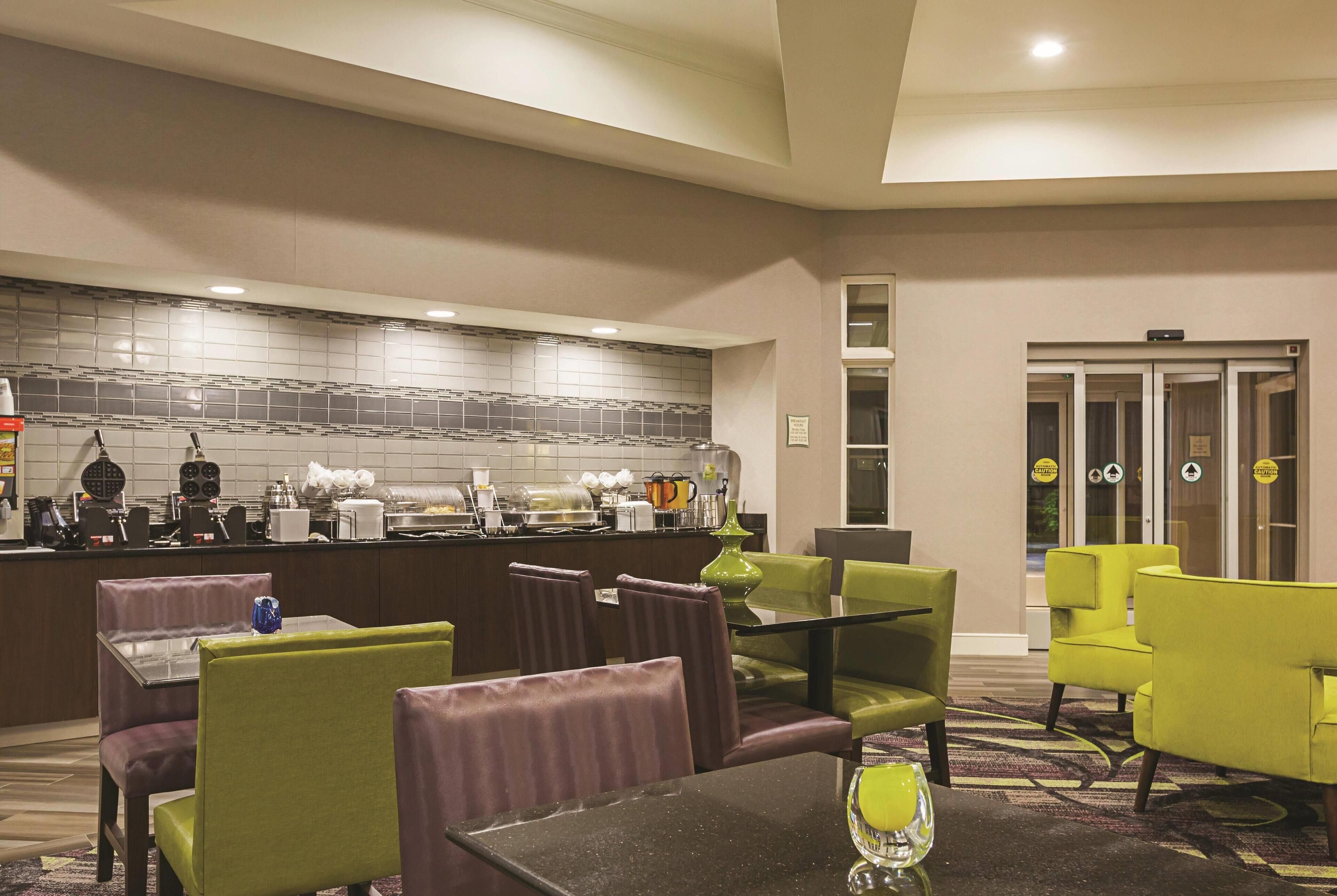 A hotel lobby with a bar area, seating with purple and green chairs, and a tiled backsplash.