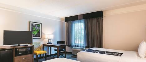 A hotel room with two beds, a desk, a television, and a window with curtains.
