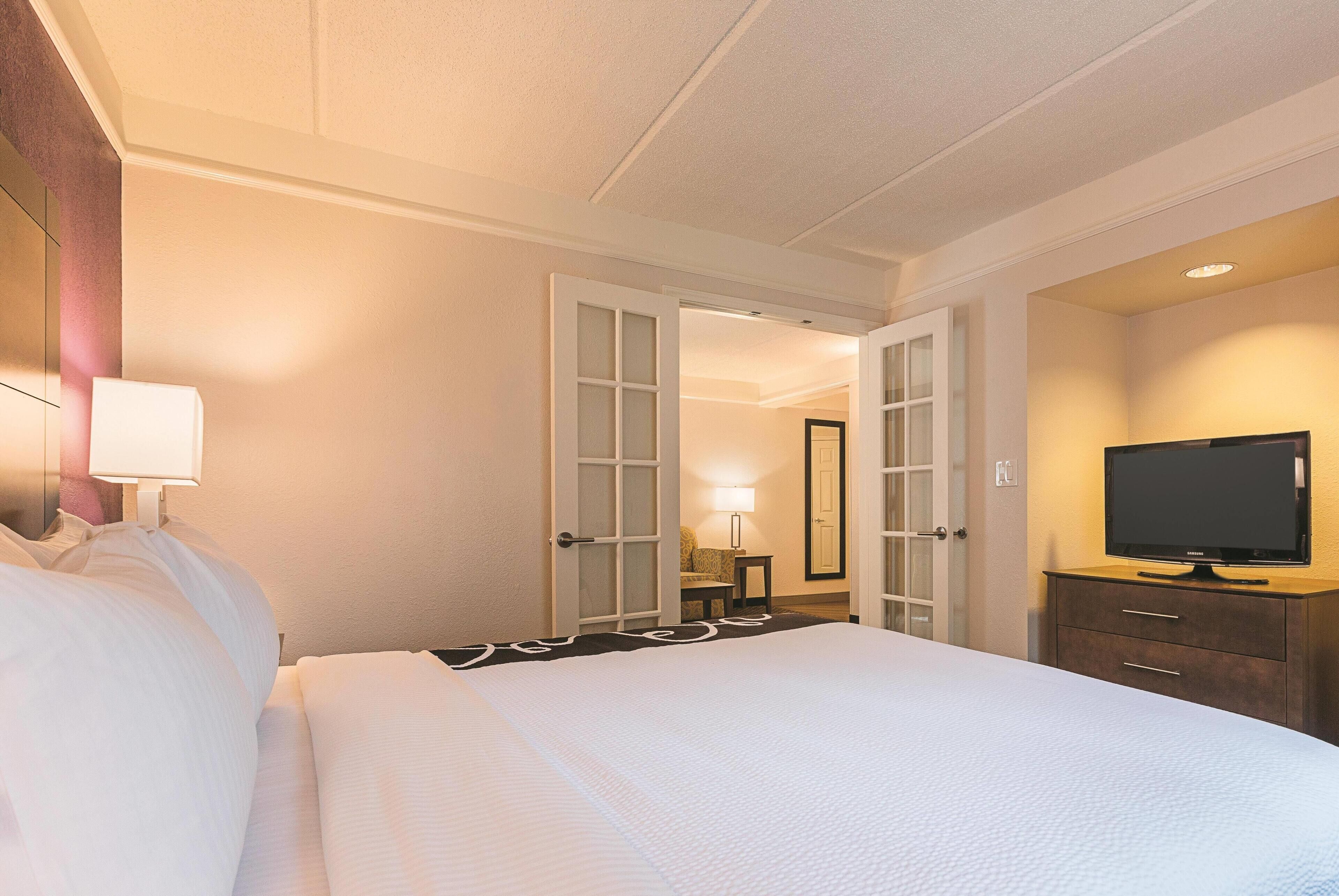 Ein Hotelzimmer mit einem großen Bett, einem Fernseher auf einer Holzkabine und einer Tür zu einem weiteren Raum.