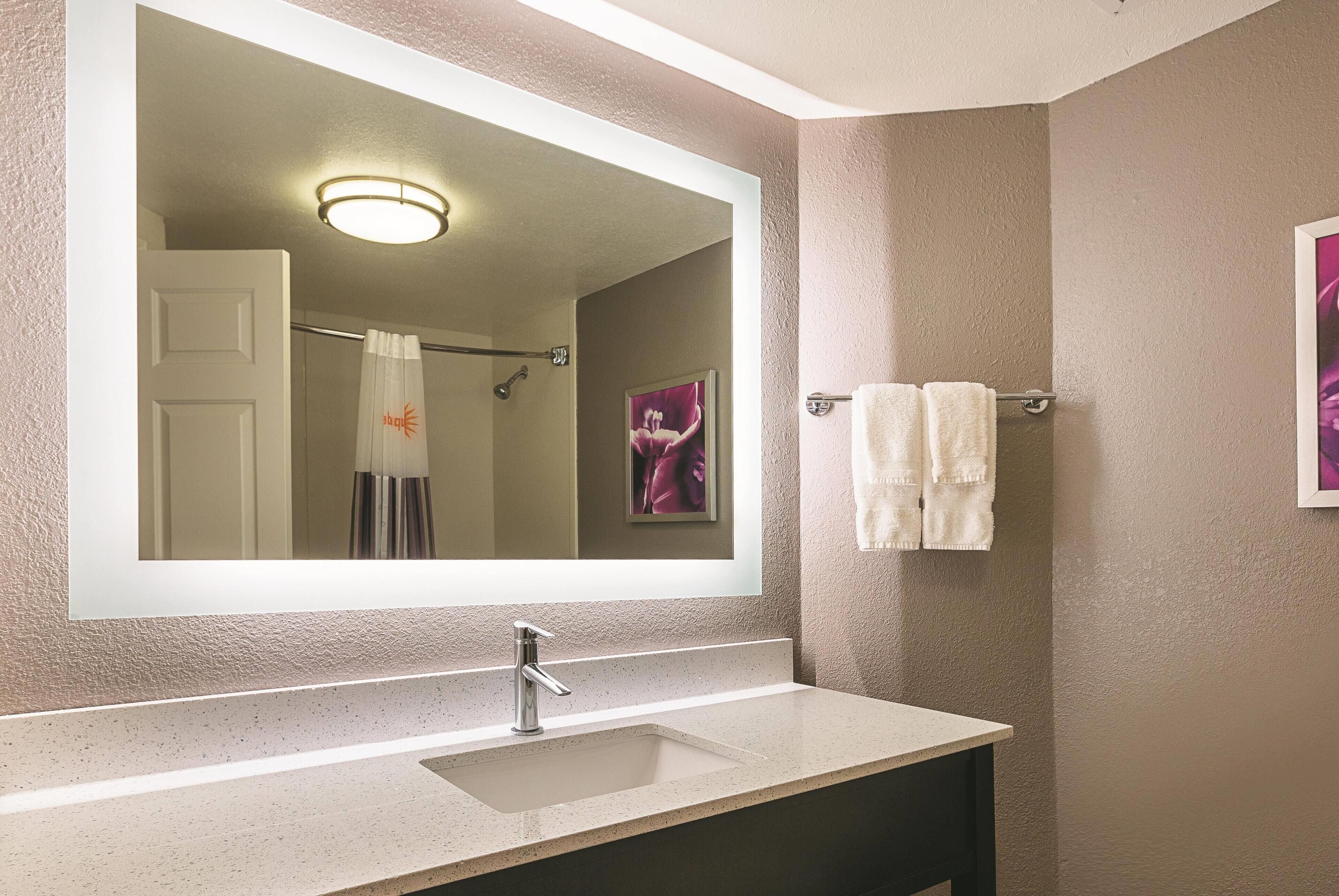 A bathroom with a large mirror, a sink, and a towel rack.