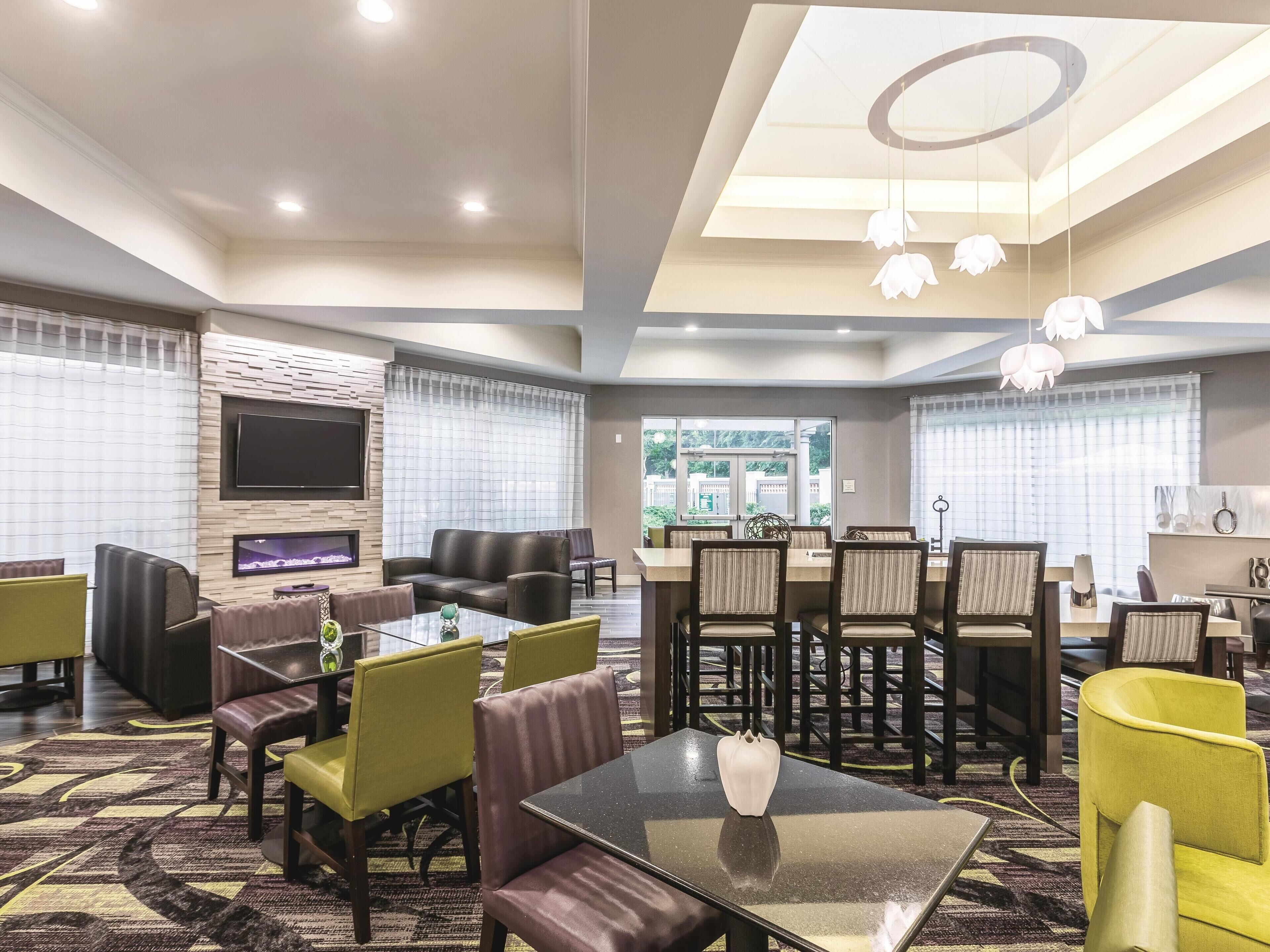 A modern hotel lobby with a seating area, a dining table, and a TV screen.