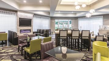 A modern hotel lobby with a seating area, a dining table, and a TV screen.