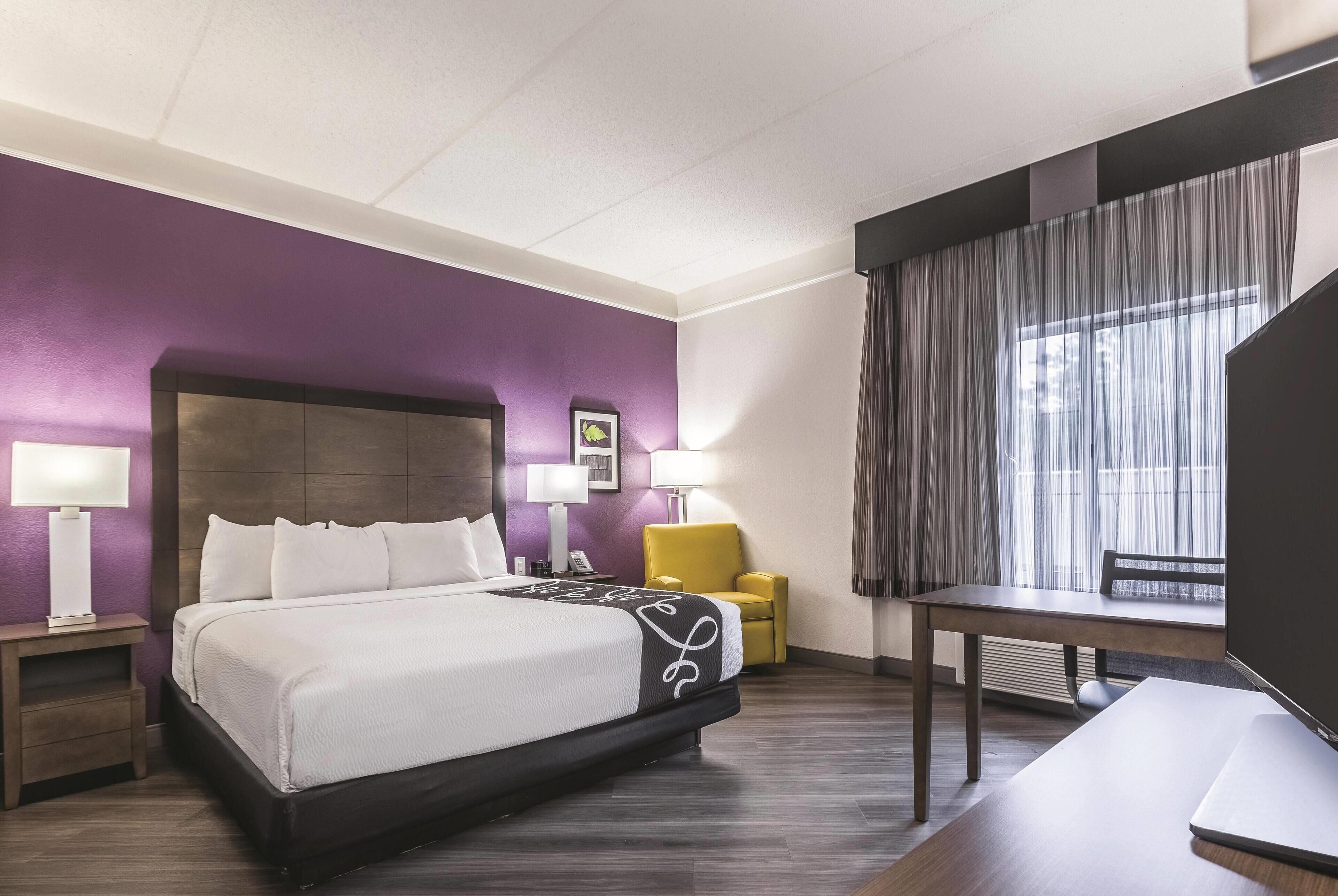 A hotel room with a large bed, a desk, a chair, and a window with curtains.