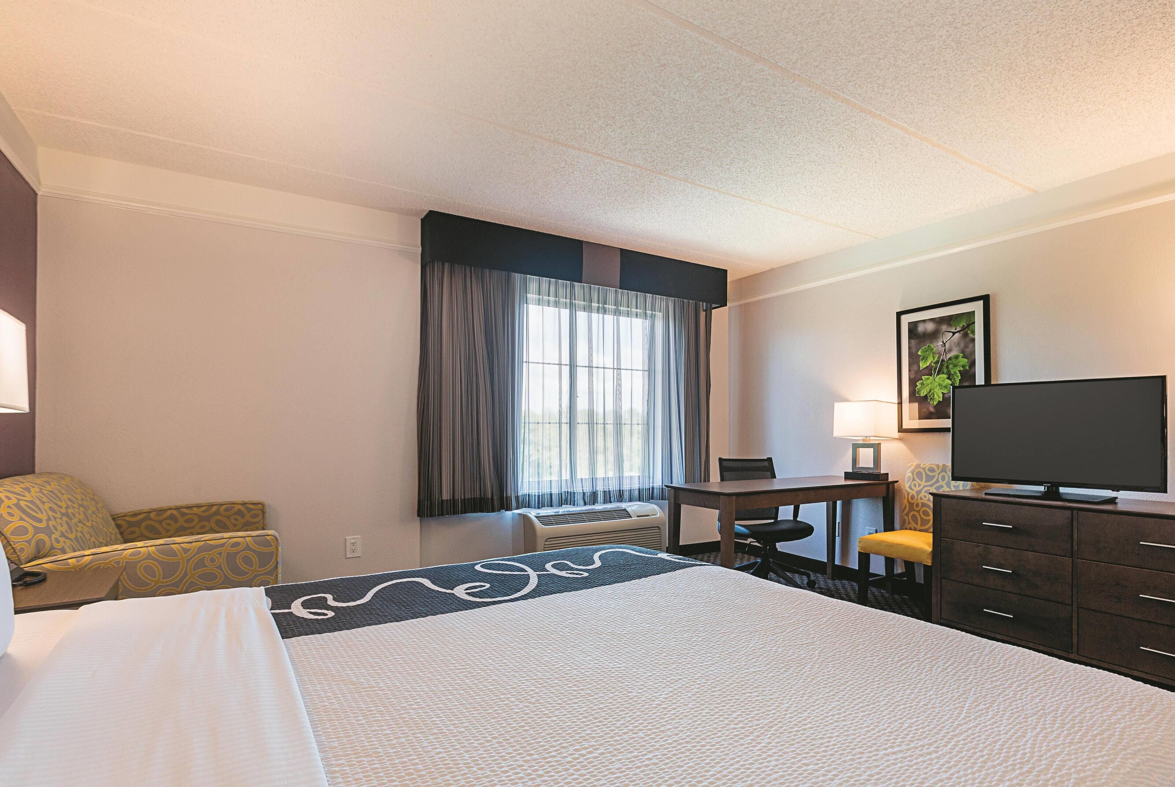 A hotel room with a large bed, a desk, a chair, a television, and a window with curtains.