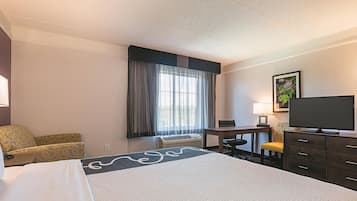 A hotel room with a large bed, a desk, a chair, a television, and a window with curtains.