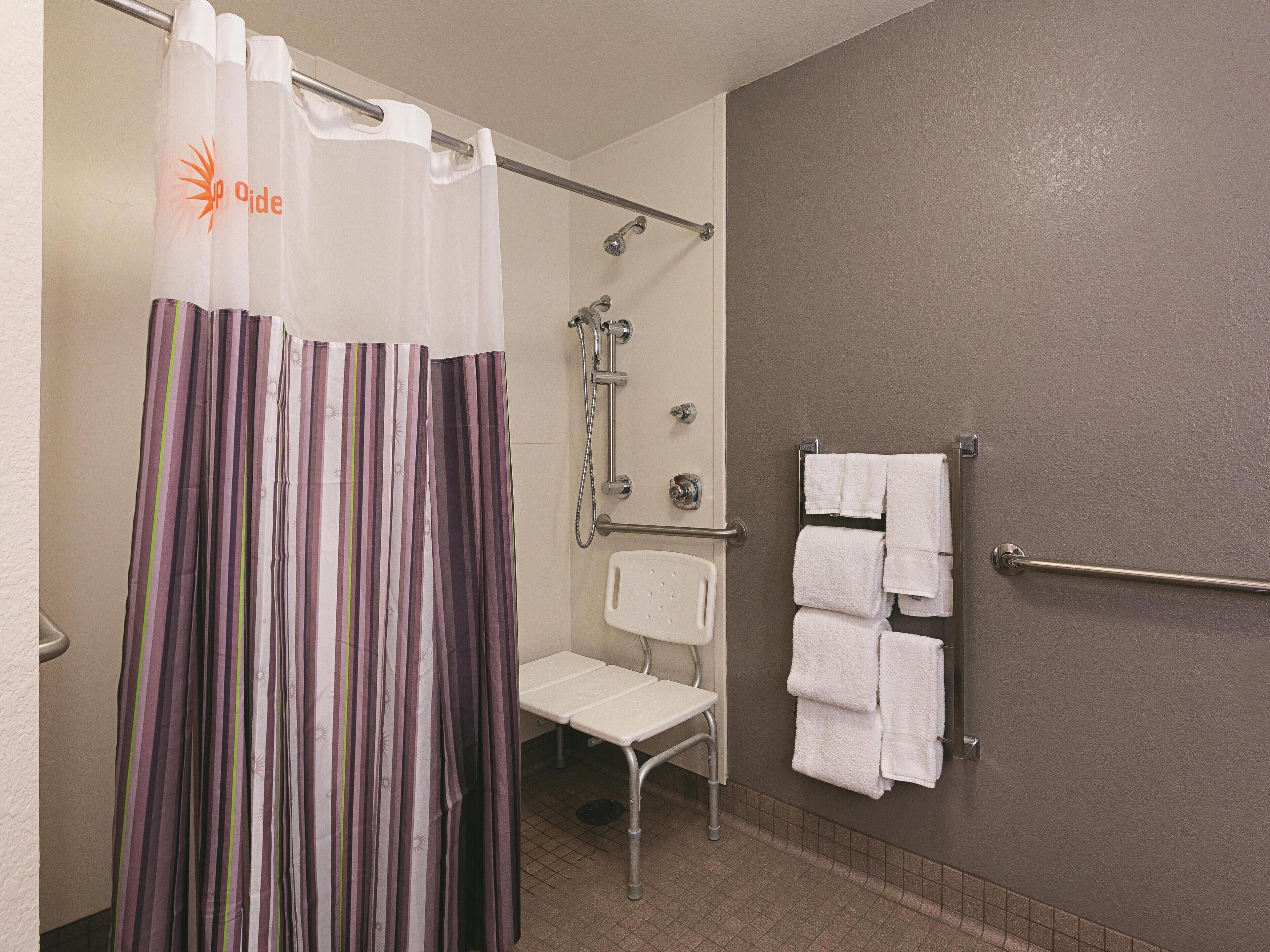 A bathroom with a shower curtain, a white chair, and a towel rack with multiple towels.