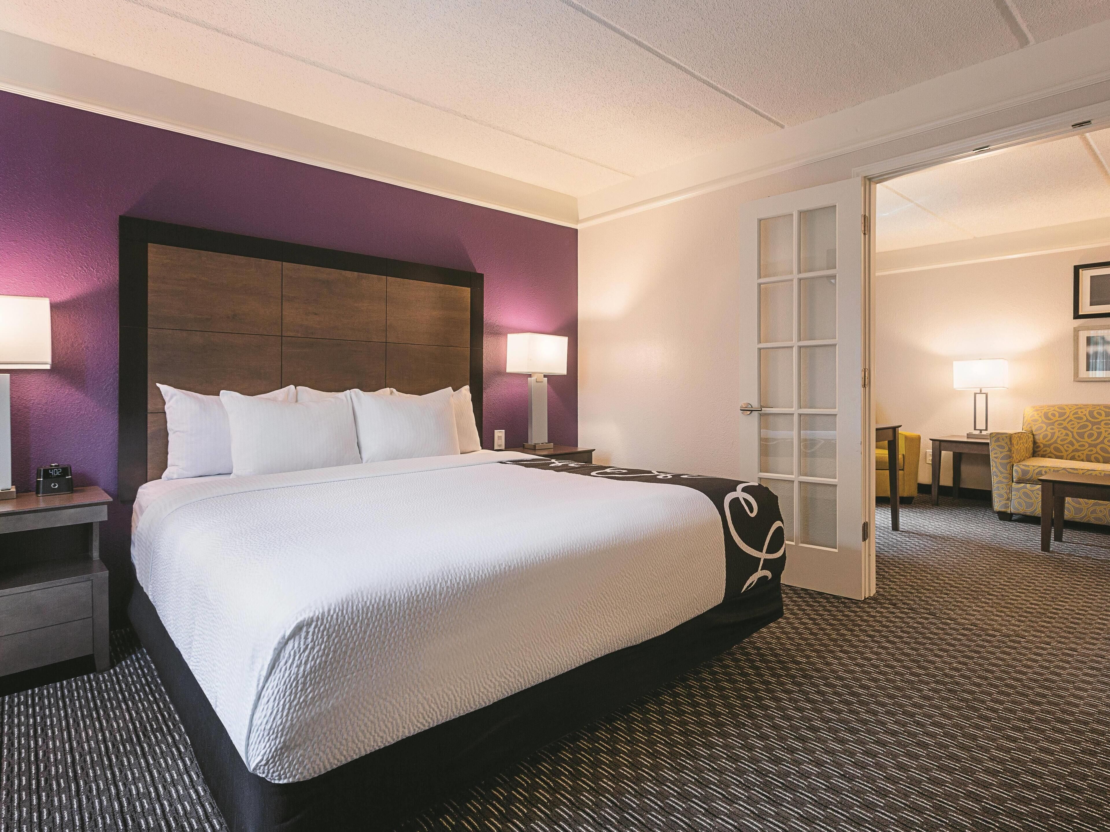A hotel room with a large bed, two bedside tables, a nightstand, a chair, and a desk with a lamp.