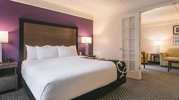 A hotel room with a large bed, two bedside tables, a nightstand, a chair, and a desk with a lamp.