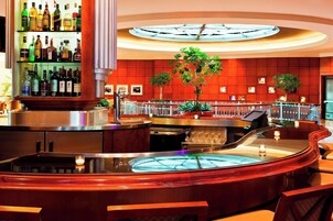 A bar area with a large clock, shelves of liquor bottles, and potted plants.