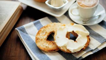 A table with a bagel, a cup of coffee, and a small dish of cream cheese.