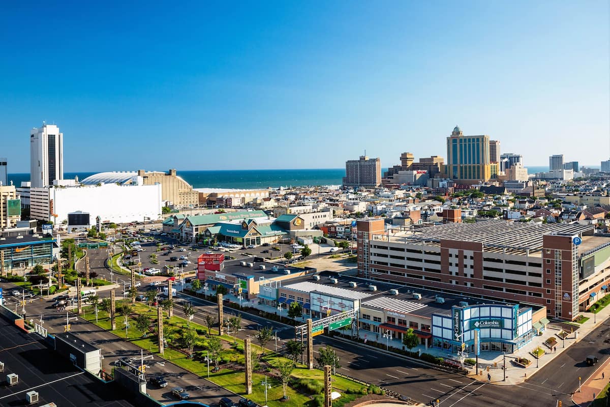 A cityscape with a prominent building with a blue and white facade, a large parking structure, and a clear view of the ocean.