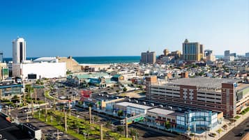 A cityscape with a prominent building with a blue and white facade, a large parking structure, and a clear view of the ocean.