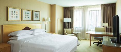 Habitación de hotel con una cama grande, un escritorio con una silla, un televisor y cuadros en la pared.
