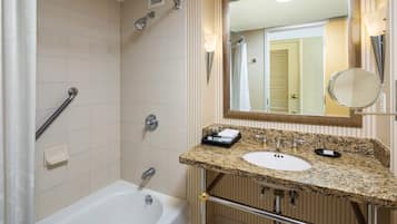 A bathroom with a white bathtub, a granite countertop sink, a large mirror, and a shower with a handheld showerhead.
