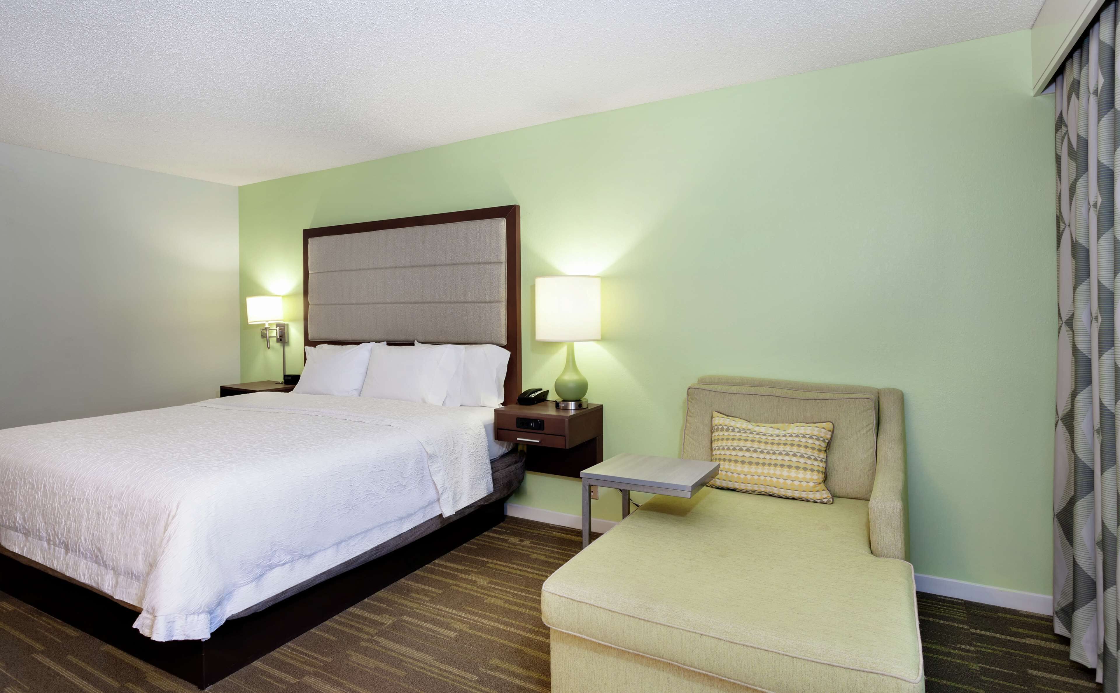 A hotel room with a large bed, a bedside table with a lamp, a small sofa, and a patterned curtain.