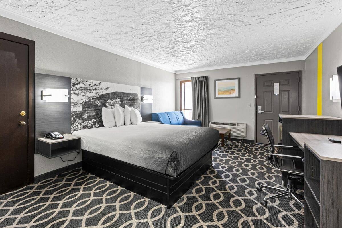 Ein Hotelzimmer mit Bett, Nachttisch, Lampe und Schreibtisch mit Stuhl.