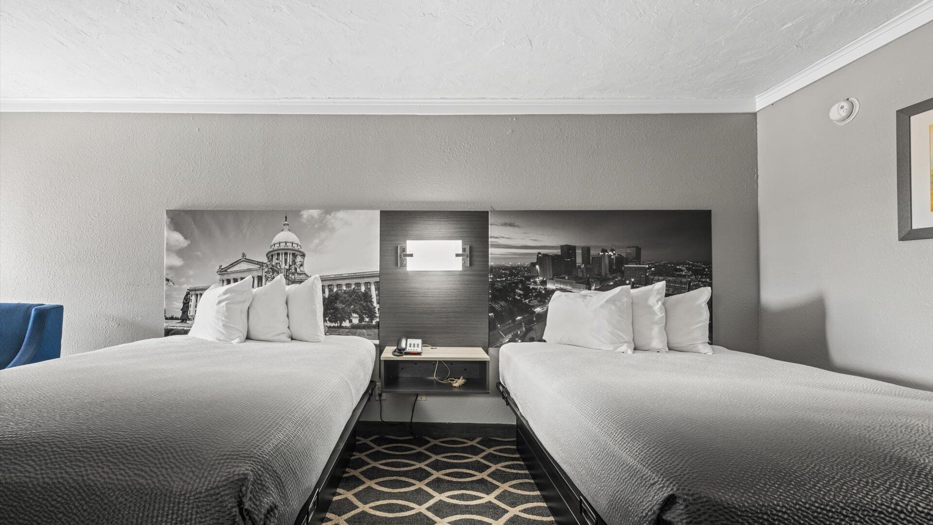 A hotel room with two beds, a nightstand, a lamp, and a cityscape view.