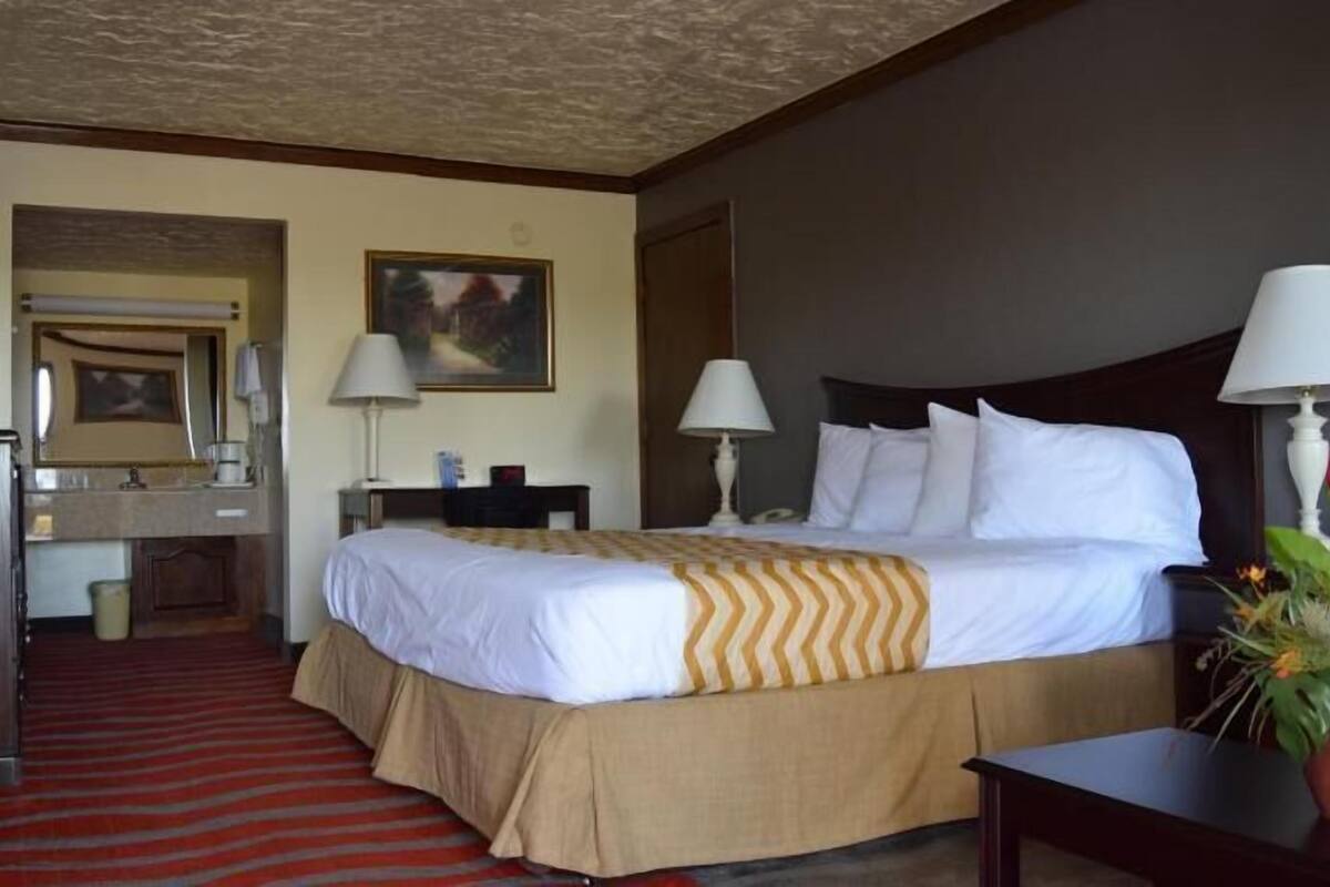Ein Hotelzimmer mit Bett, Nachttischlampen, Schreibtisch, Stuhl, Spiegel und einem Bild an der Wand.