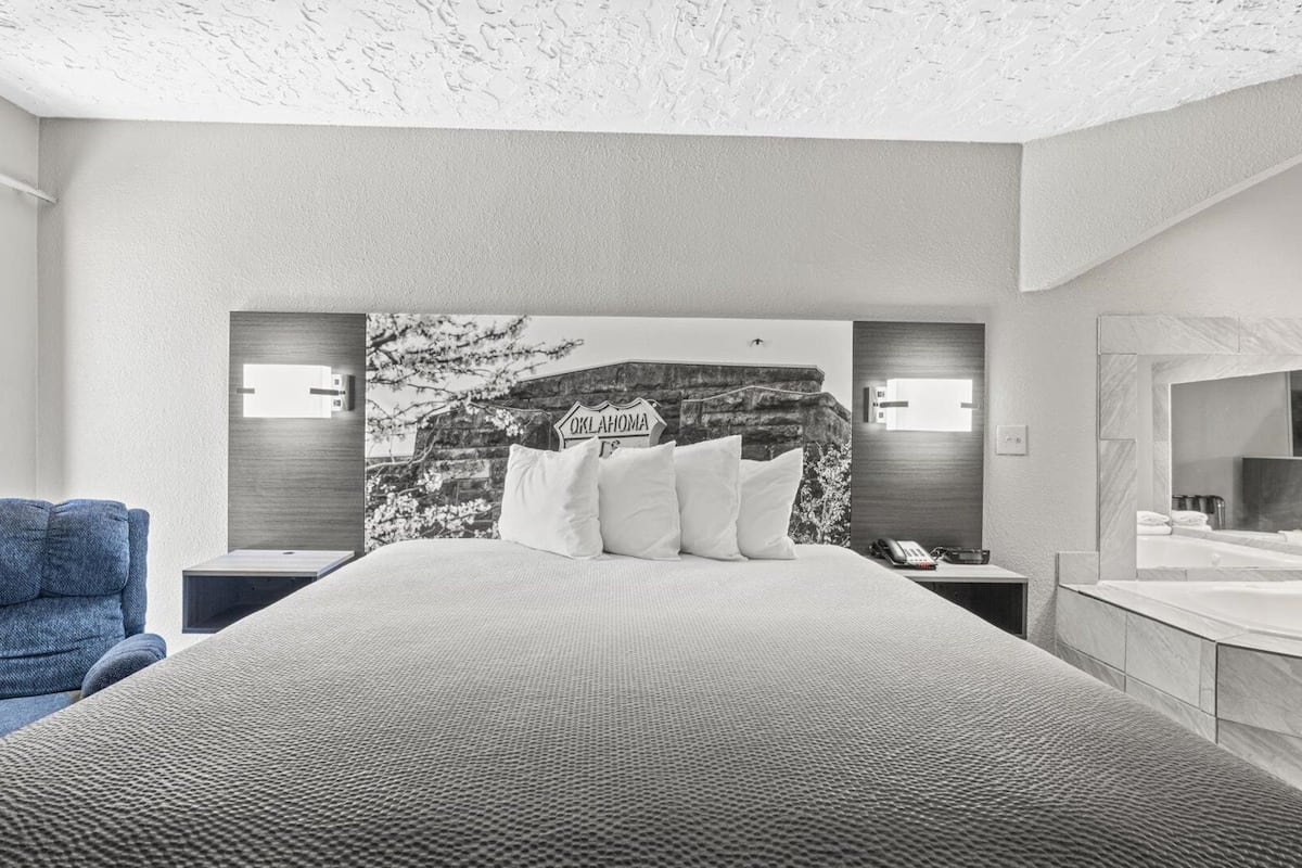 Ein modernes Hotelzimmer mit einem großen Bett, einem blauen Sessel, einem Nachttisch mit Telefon und einem wandmontierten Spiegel.