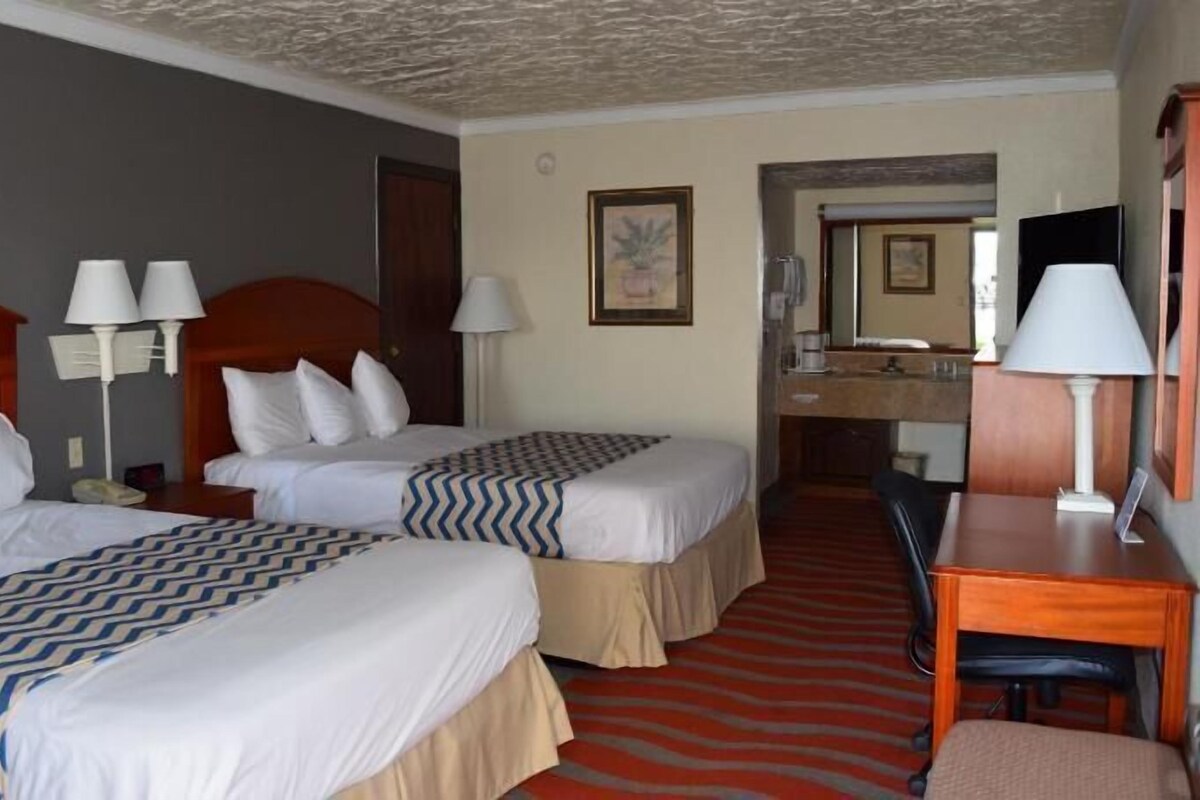 Ein Hotelzimmer mit zwei Betten, einem Schreibtisch, einem Stuhl, einem Spiegel und einem roten Teppich.