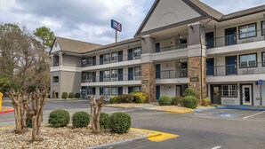 Un hotel a più piani con un cartello ben visibile che riporta 'Hotel Lobby', un parcheggio con posti riservati ai disabili e un cielo sereno.