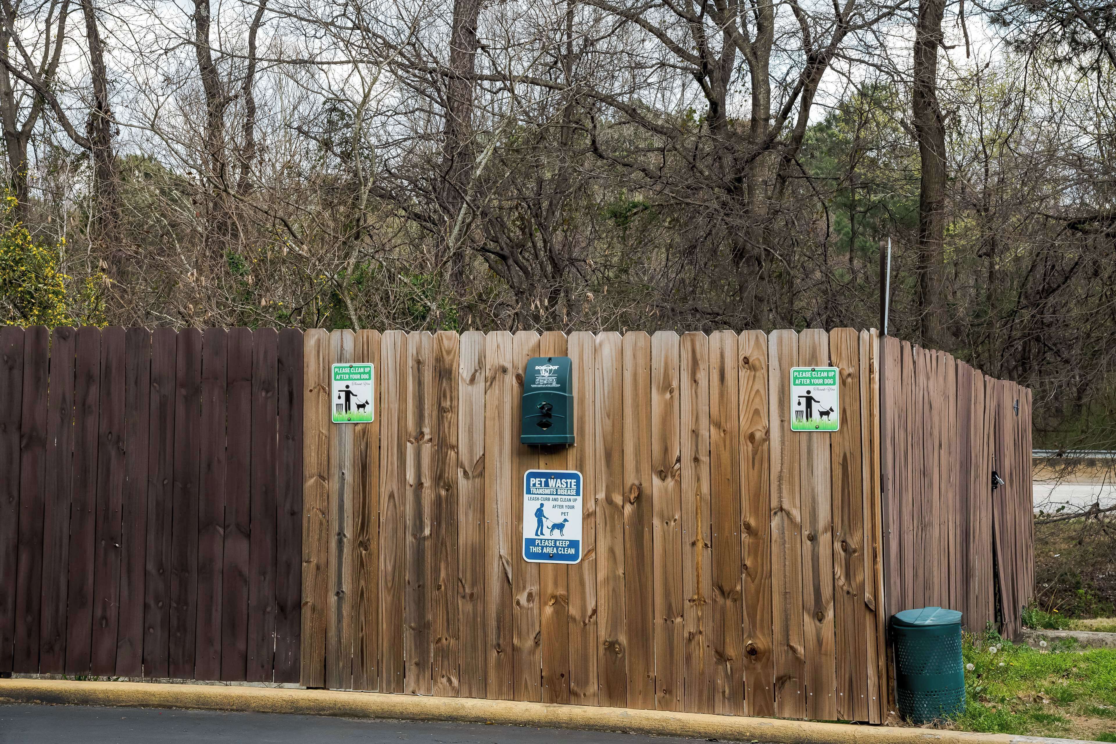 A wooden fence with two green signs indicating pet waste disposal and a trash bin.
