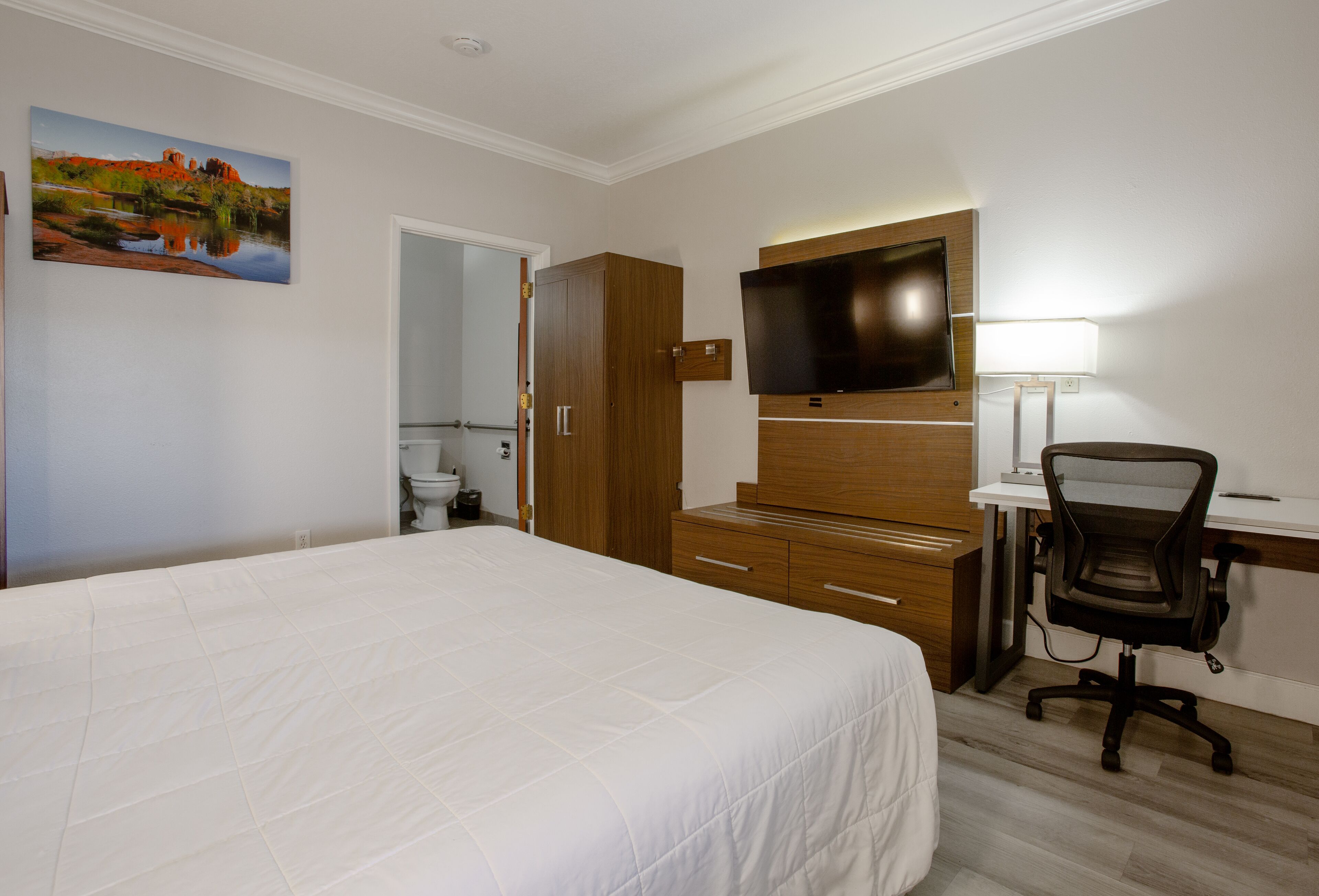 A hotel room with a large bed, a desk with a chair, a television, and a painting on the wall.