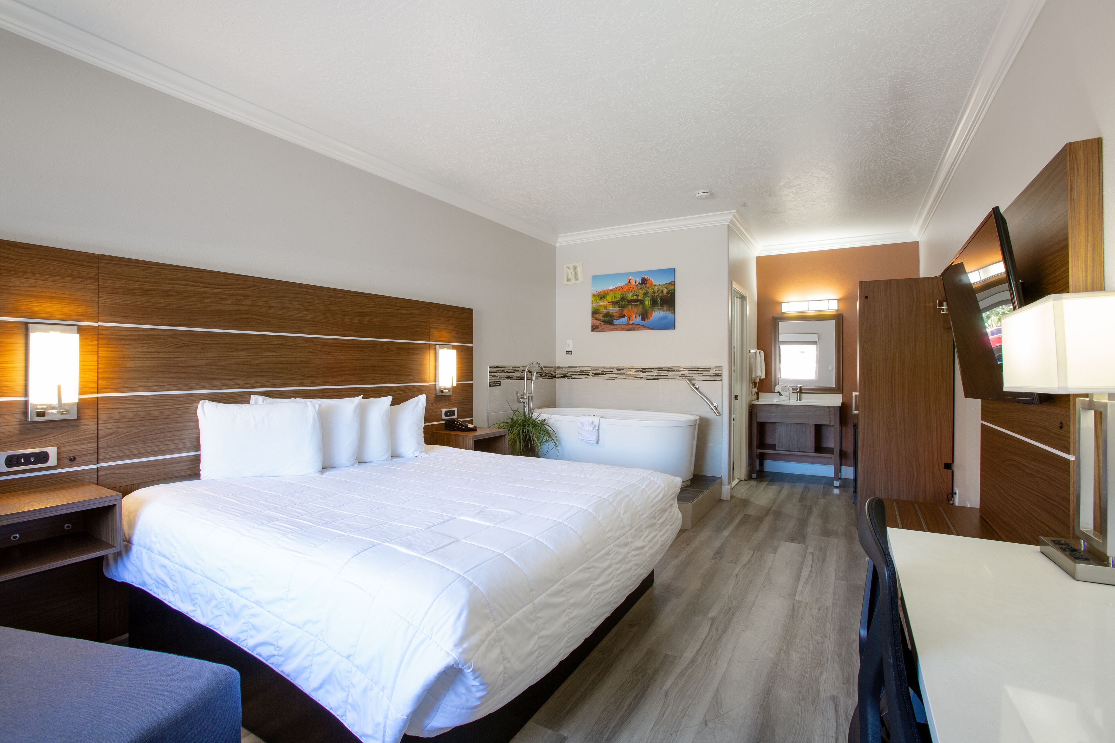 A hotel room with a large bed, a bathroom with a bathtub, a desk, and a TV.