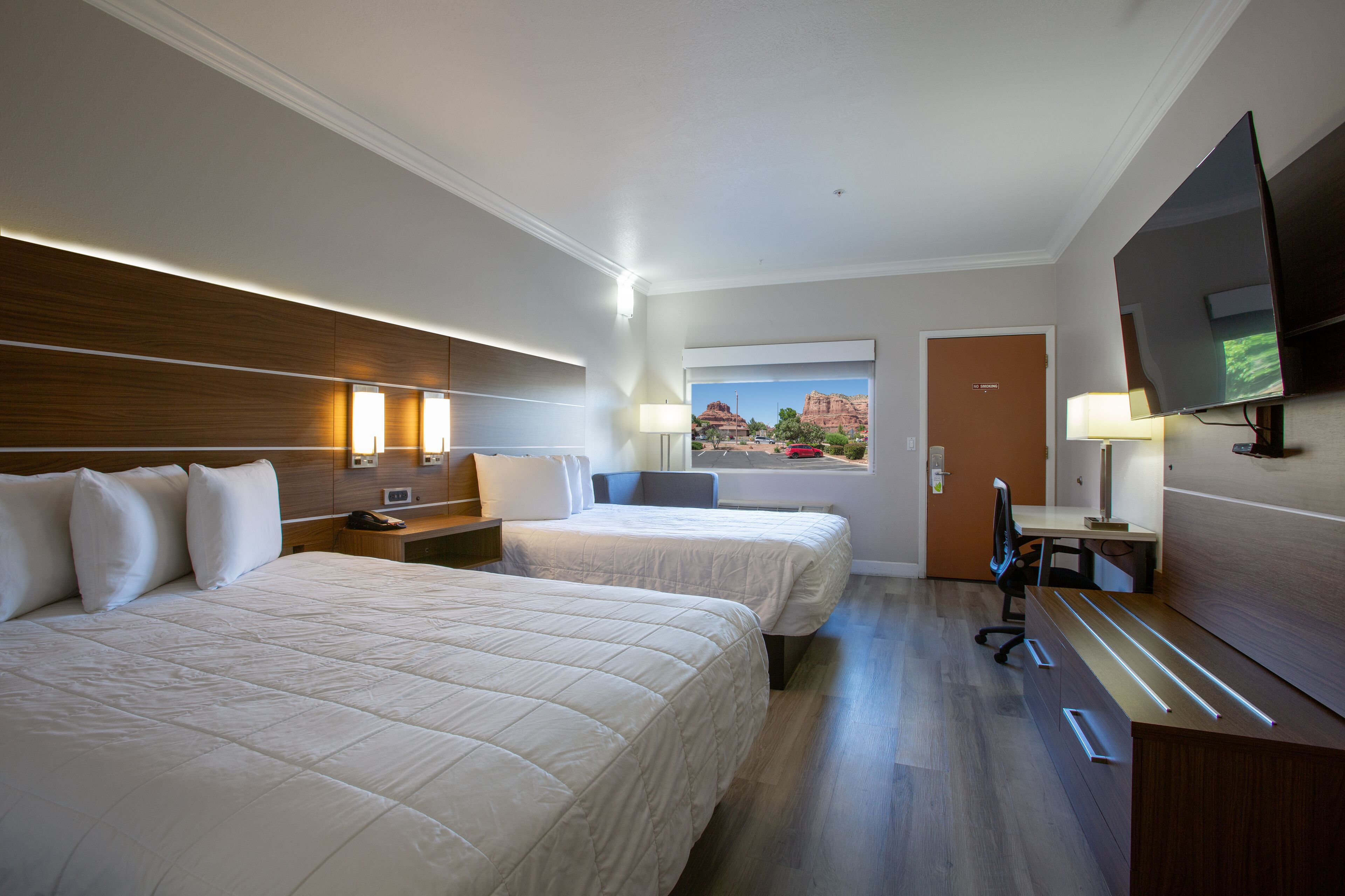 A hotel room with two beds, a desk, a chair, a TV, and a window with a view of a mountain.