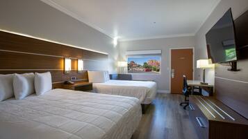 A hotel room with two beds, a desk, a chair, a TV, and a window with a view of a mountain.