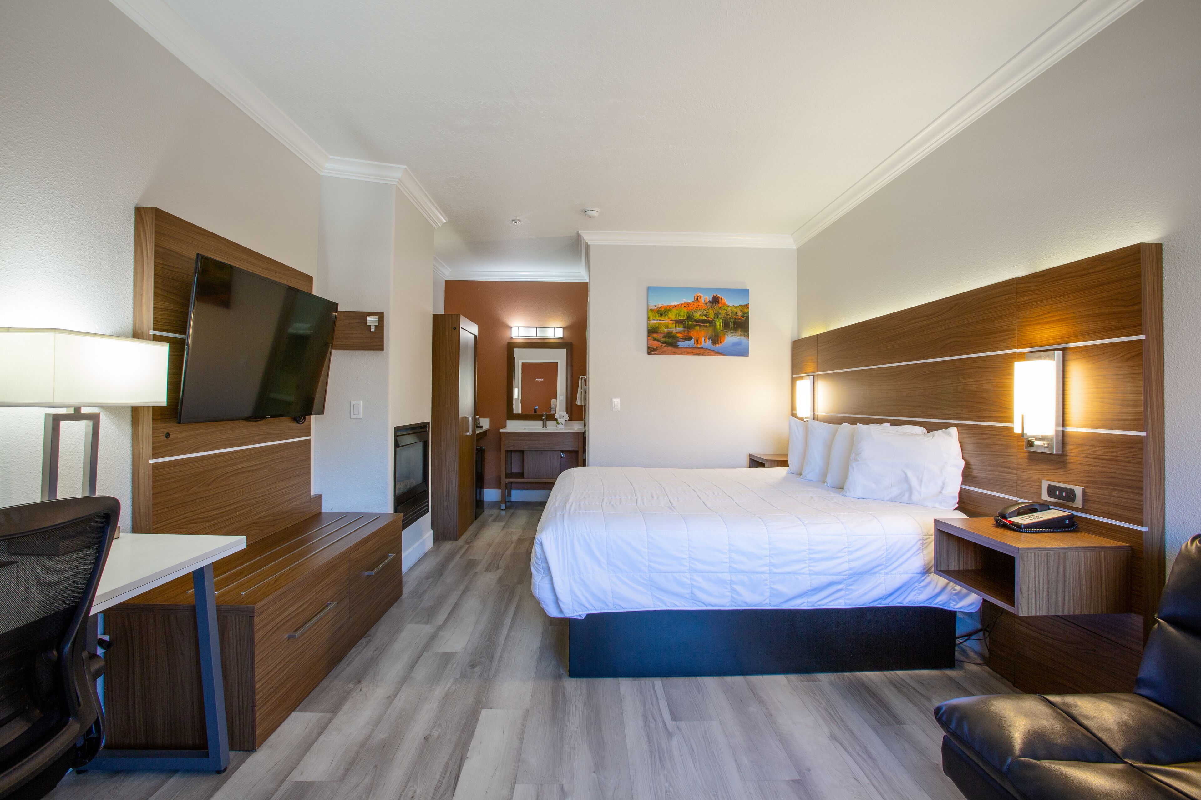 A hotel room with a bed, a desk, a chair, a TV, and a painting on the wall.