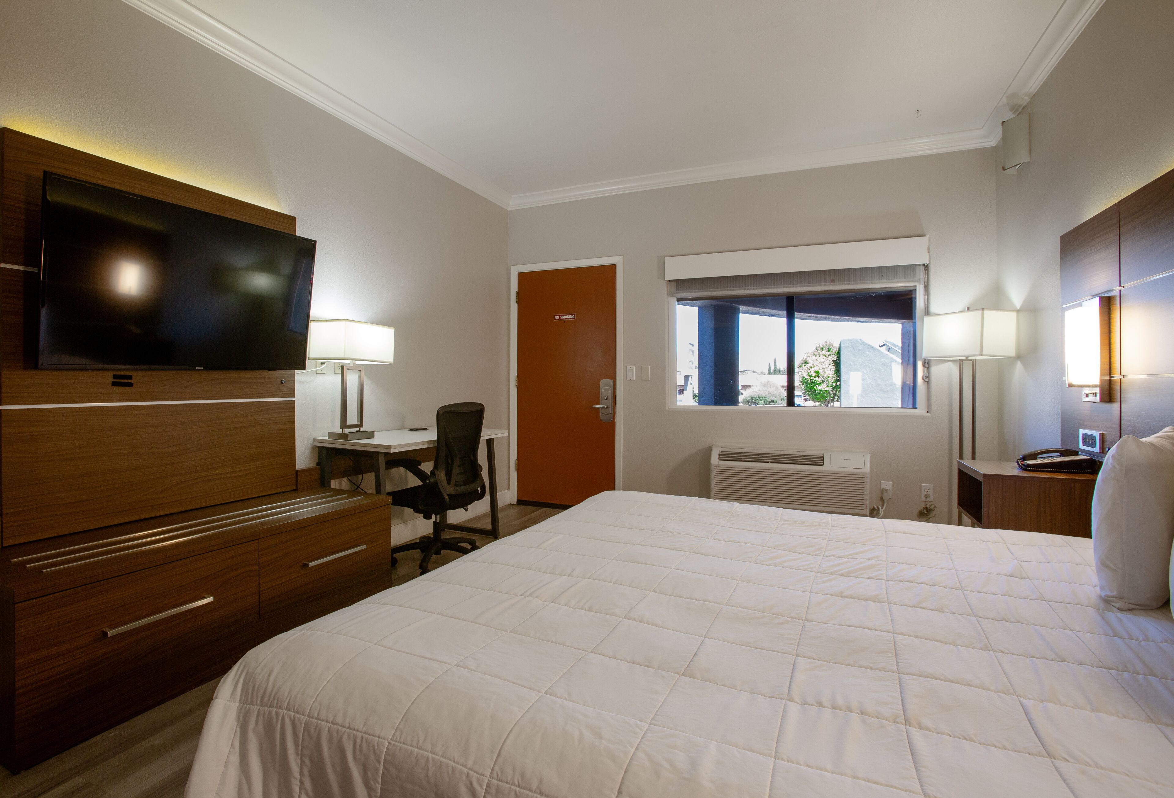 A hotel room with a large bed, a desk with a chair, a television, and a window with a view.
