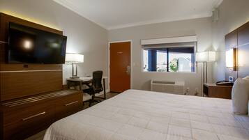 A hotel room with a large bed, a desk with a chair, a television, and a window with a view.