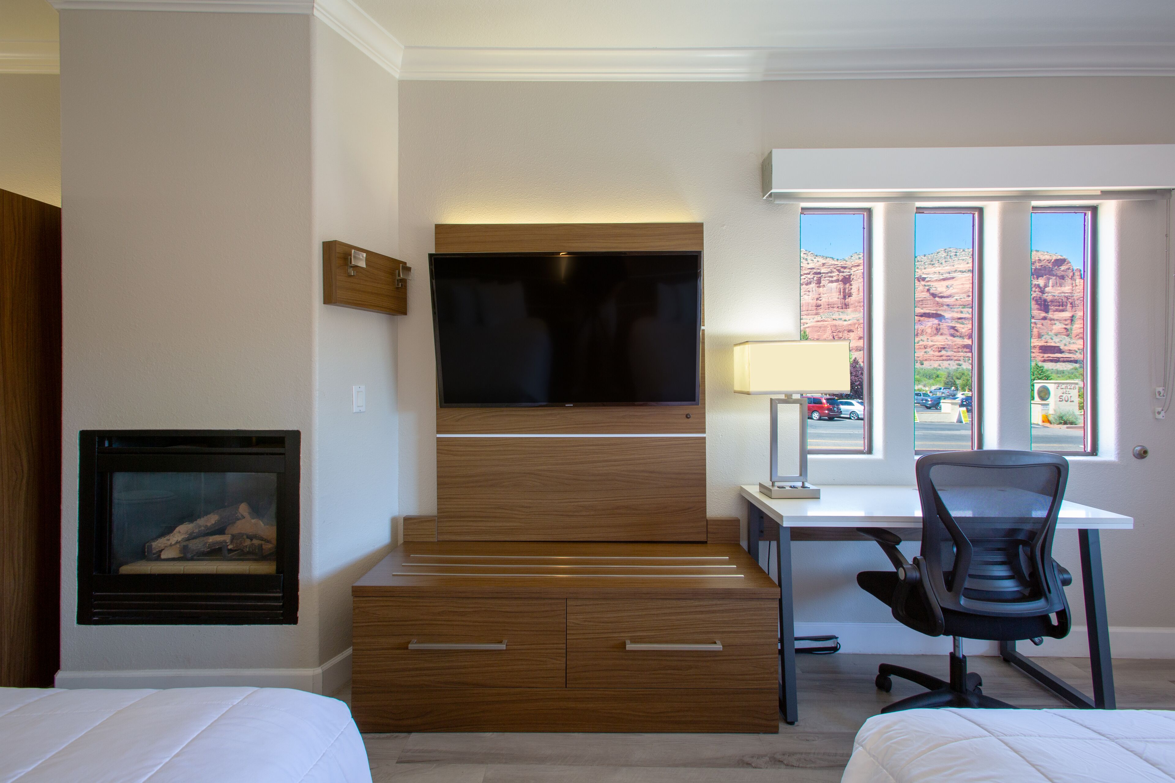 A hotel room with a bed, a desk, a chair, a TV, and a fireplace.