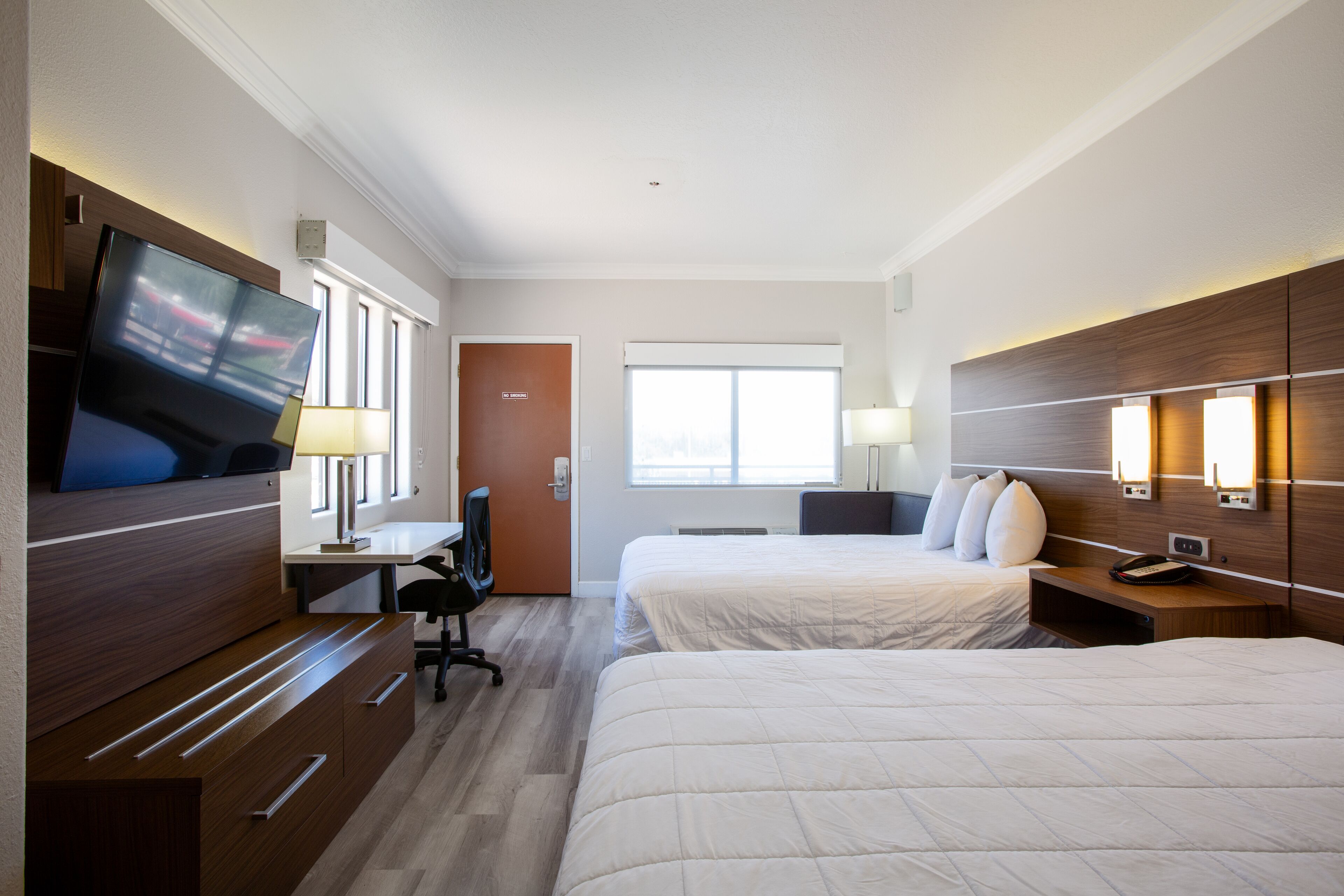Ein Hotelzimmer mit zwei Betten, einem Schreibtisch, einem Sessel, einem Fernseher und einem Fenster.