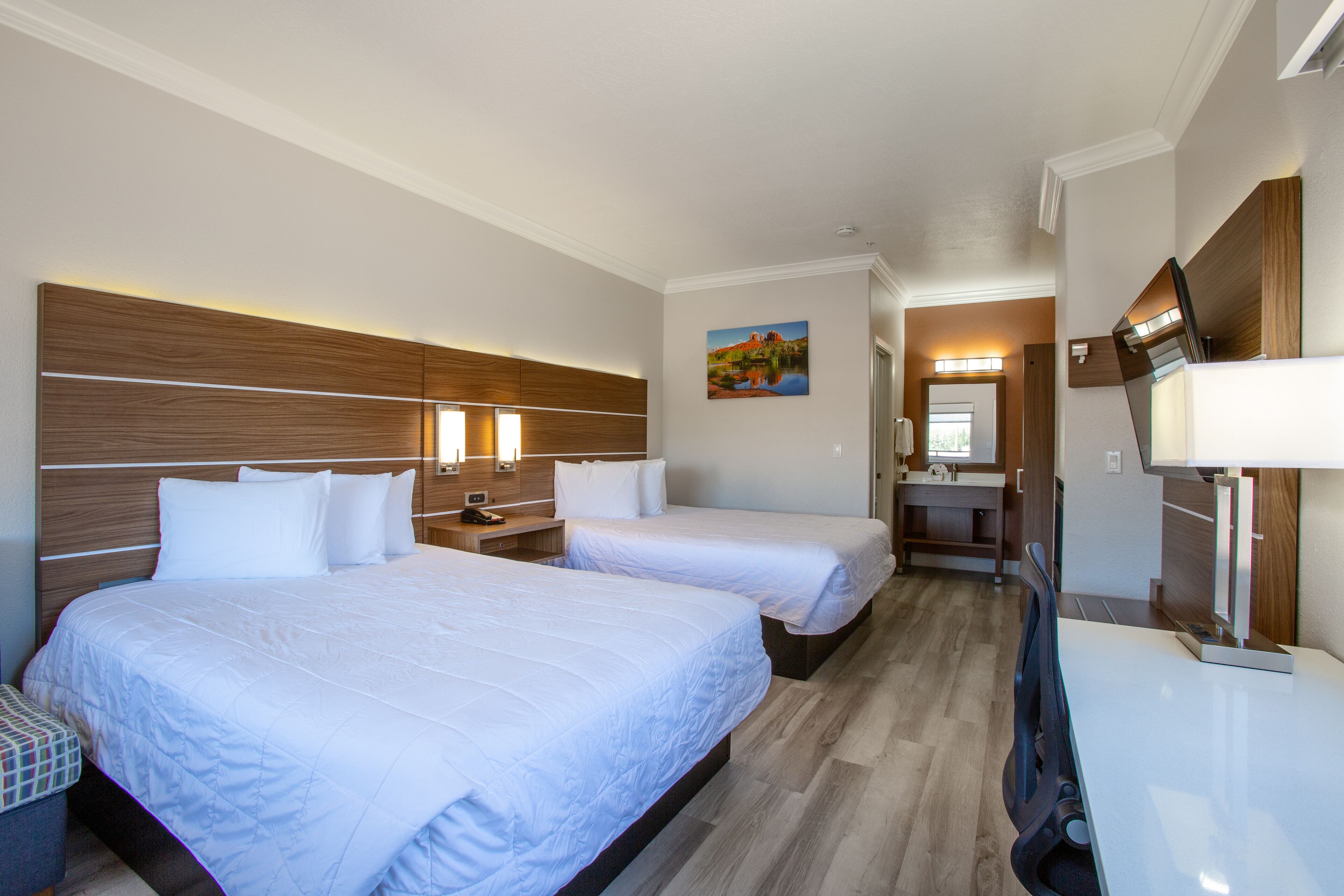 Habitación de hotel con dos camas, cabecera de madera, mesitas de noche, un televisor y un cuadro en la pared.