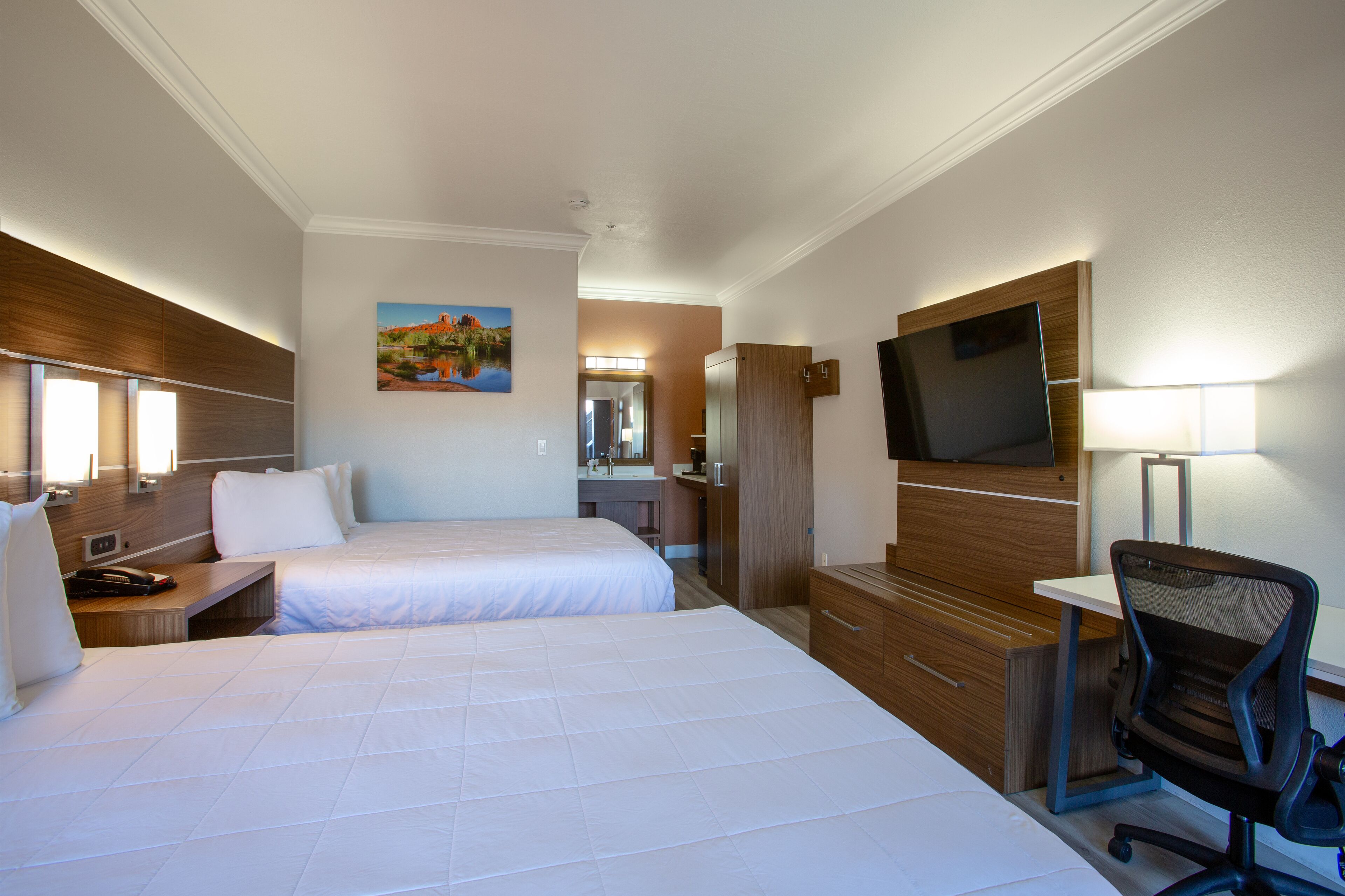 Ett hotellrum med två sängar, ett skrivbord, en stol, en tv och en tavla på väggen.