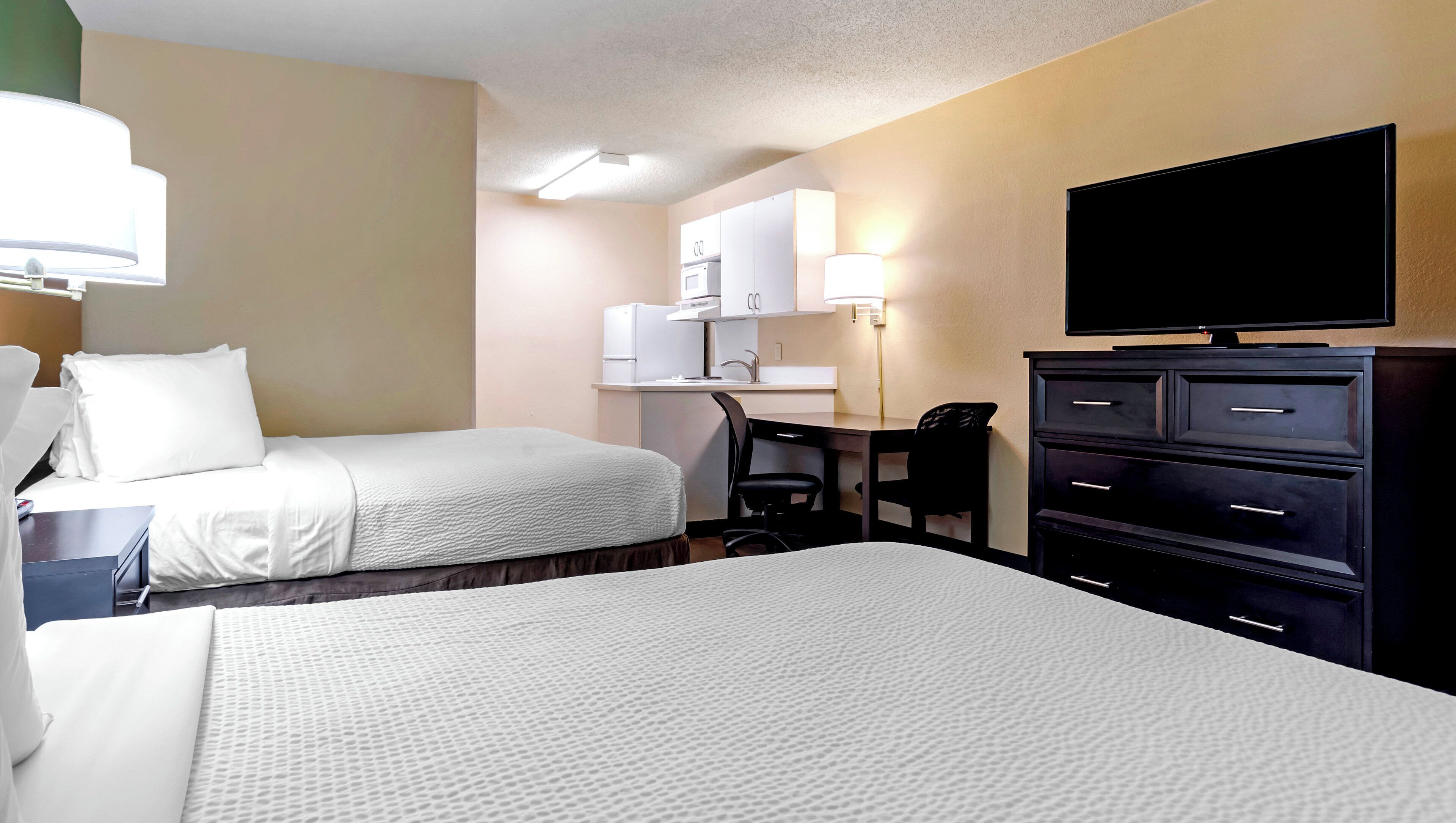 A hotel room with two beds, a desk, a chair, a television, and a minibar.
