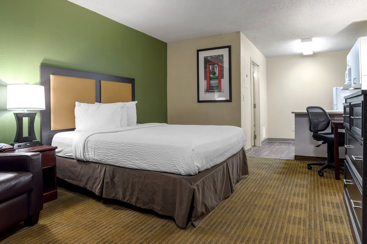 A hotel room with a bed, a desk, a chair, a television, and a telephone.