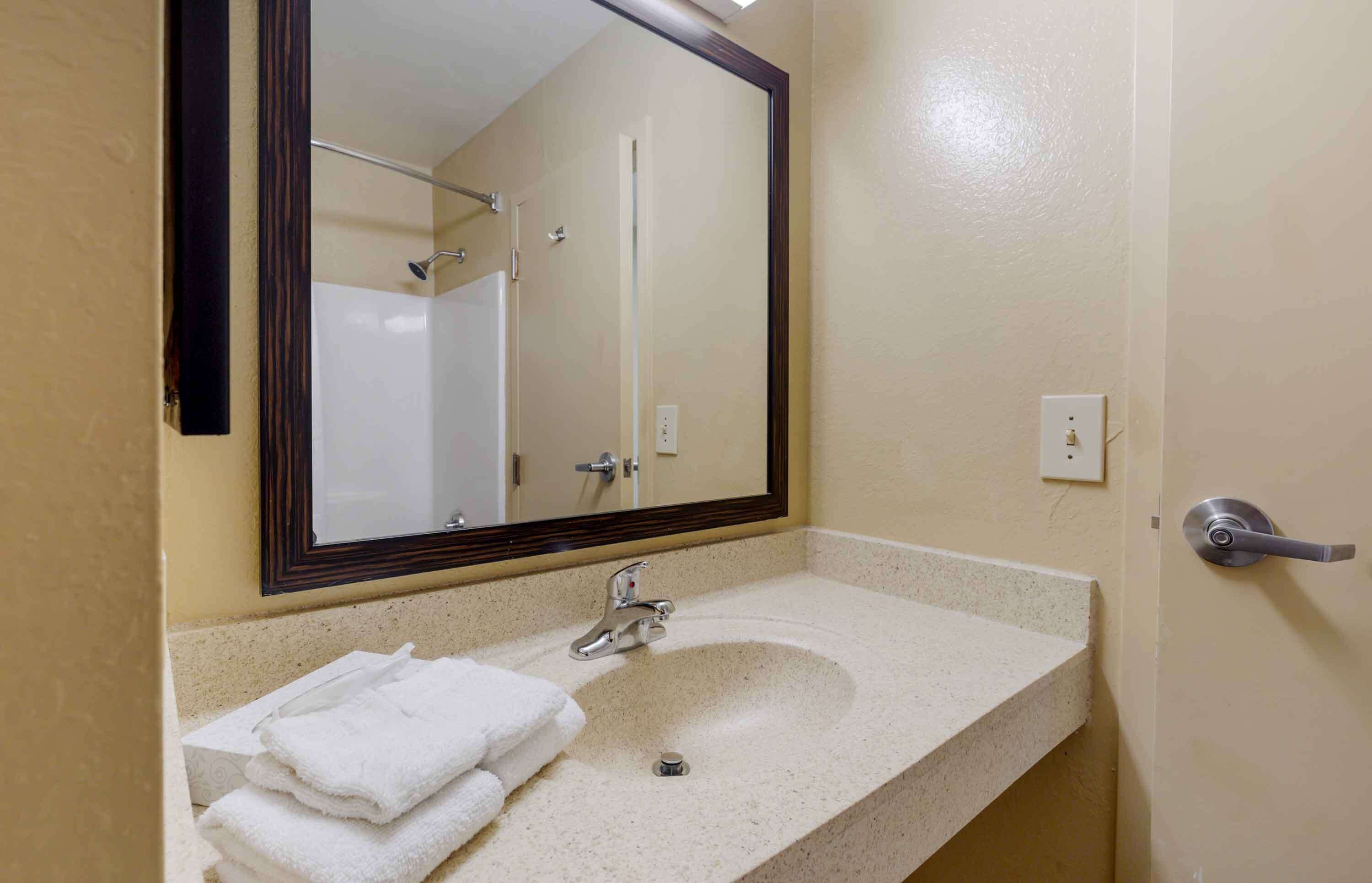 A bathroom with a sink, mirror, and towel stack.