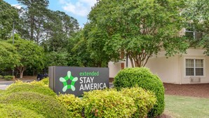 A sign for Extended Stay America with a logo, surrounded by well-maintained bushes and trees. - Extended Stay America Select Suites Fayetteville Owen Dr (Fayetteville)