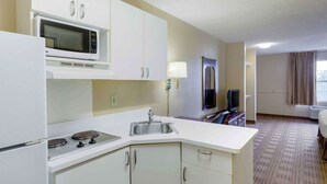 A compact hotel room with a kitchenette including a microwave, stove, sink, and cabinets. - Extended Stay America Select Suites Fayetteville Owen Dr (Fayetteville)