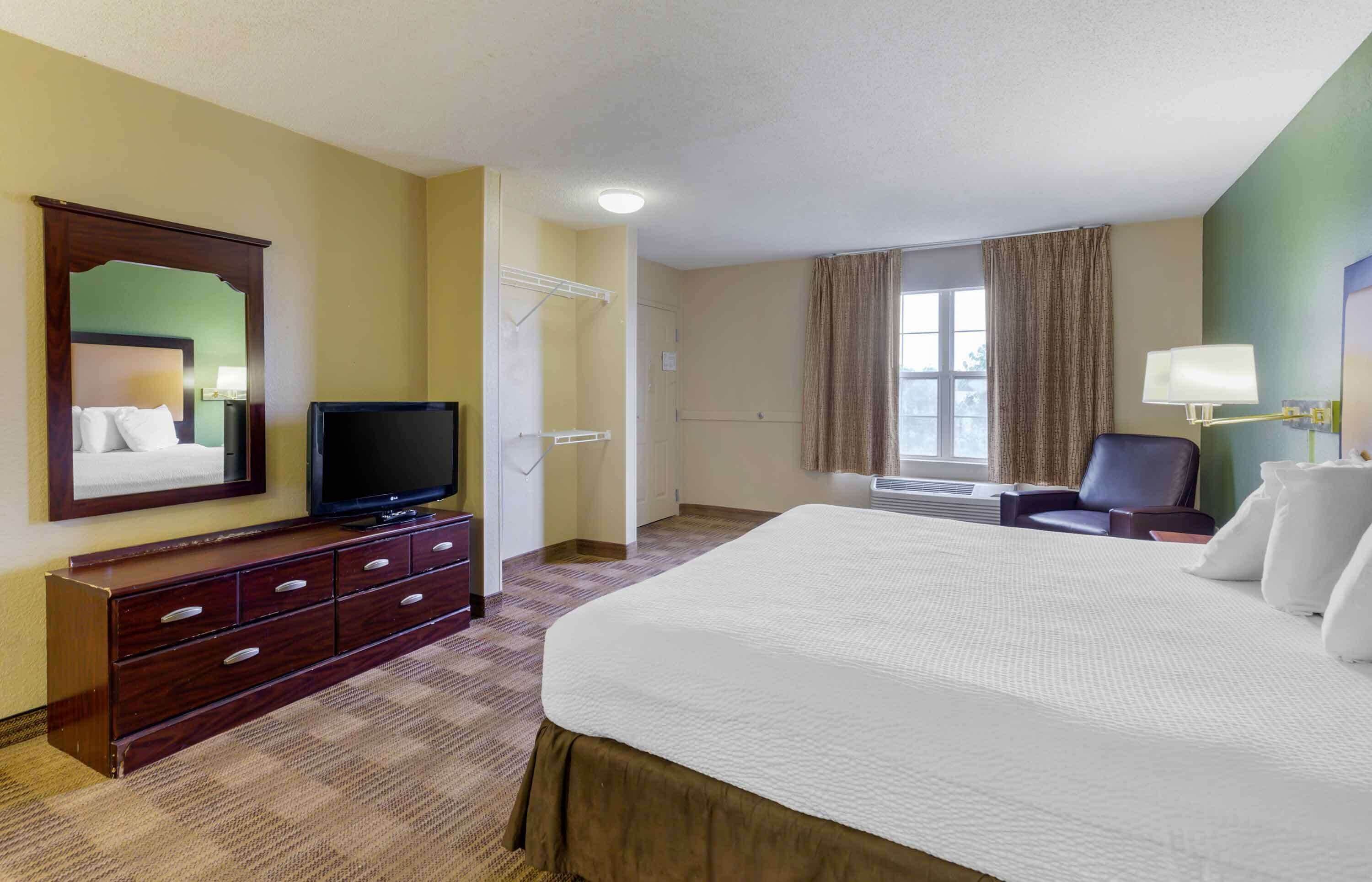 A hotel room with a large bed, a TV, a dresser, a chair, and a window with curtains.