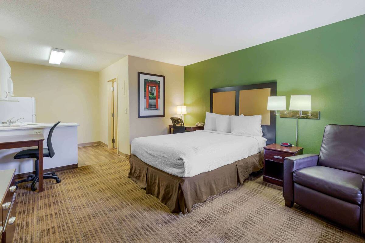 Una habitación de hotel con cama, escritorio, silla y una pared de acento verde.