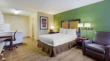 A hotel room with a bed, desk, chair, and a green accent wall.
