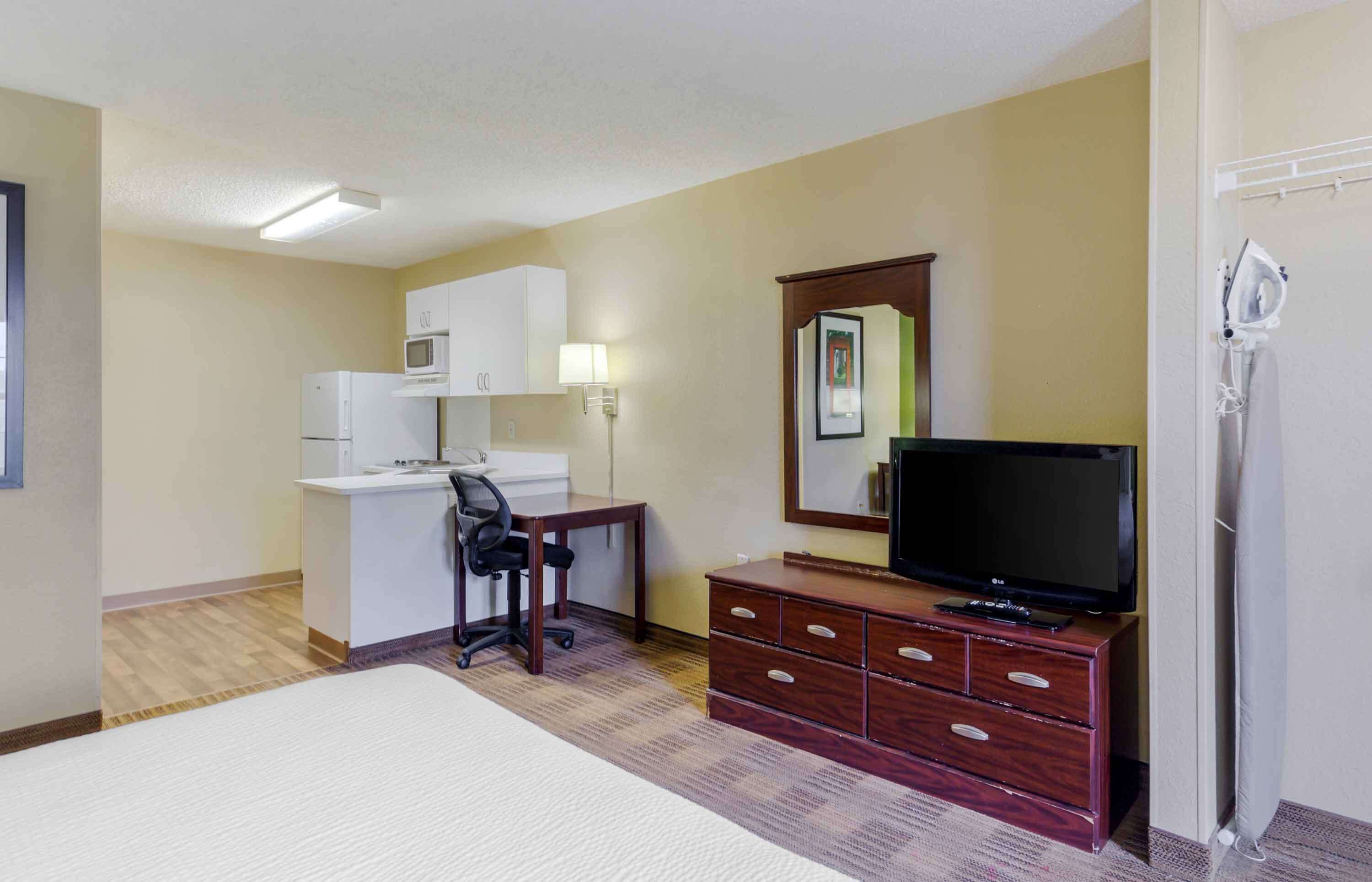 Ein Hotelzimmer mit Bett, Schreibtisch mit Stuhl, Fernseher, Kommode, Mikrowelle und Kühlschrank.