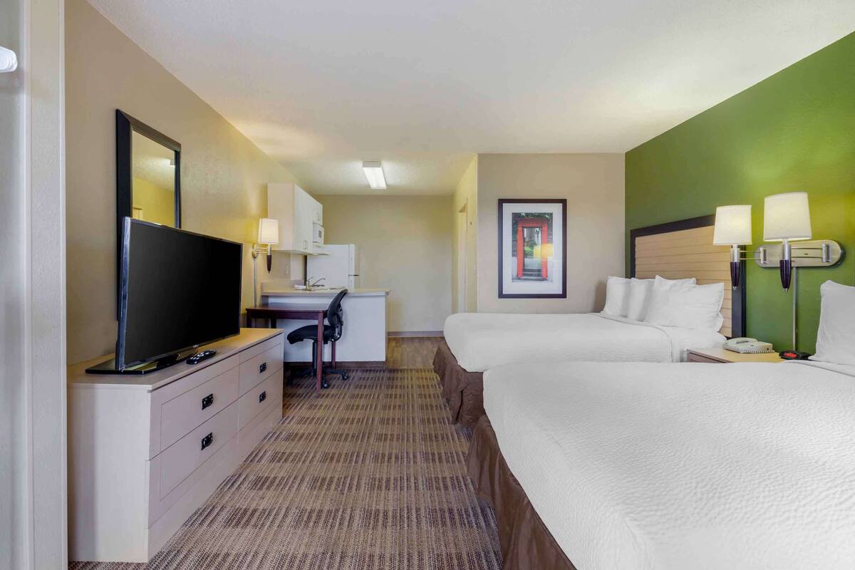 Habitación de hotel con televisión, escritorio, dos camas y una pared de acento verde.